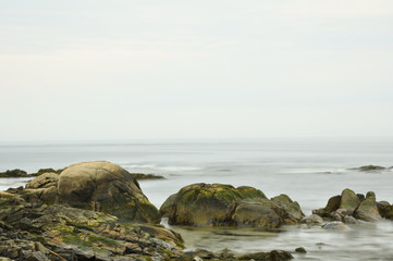 Beautiful green colored boulders by the oceans edge, and smooth silky ocean waves and blue sky for a background