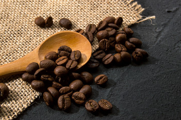 Coffee beans in burlap fabric and wooden spoon on dark concrete background