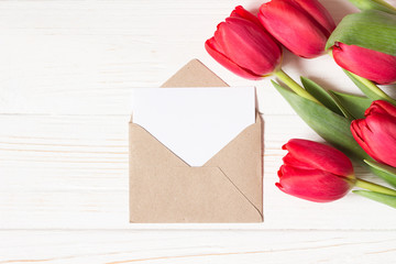 Envelope and red tulips on white wooden background. Mock up. Flat lay with copy space.