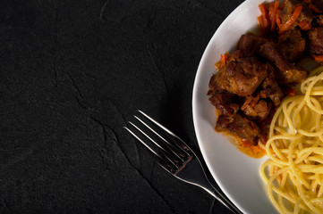 Pasta with pork meat and fork in white plate on dark cement background view top