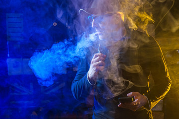 vaping man holding a mod, Vape. Men with beard in sunglasses vaping and releases a cloud of vapor.
