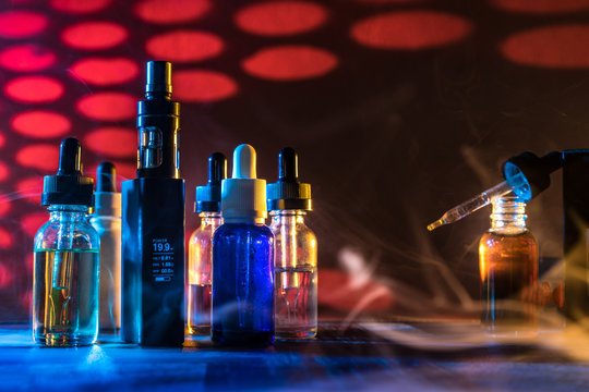 Vape. Concept of liquids for electronic cigarettes. Jars with liquids for steam. Steam on the table with an electronic cigarette.