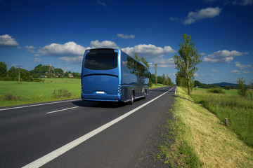 Blue bus traveling on asphalt road in a rural landscape. Village and mountain with castle ruins in the background. © am