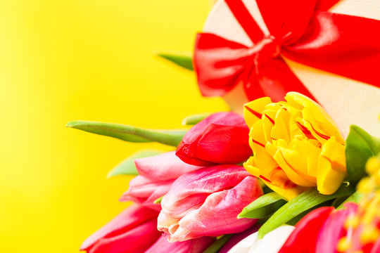 Colorful tulips flowers with decorartive giftbox on yellow background with free space. Mothersday or spring concept. Clos e up image