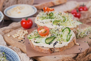 Healthy vegetarian bruschettas with bread, micro greens, hummus, cherry tomatoes, cucumbers and pine nuts