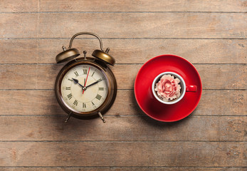 Cup of tea with rosebud in it and alarm clock