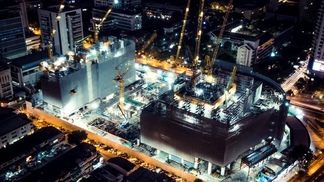Time-lapse of construction site at night with light trails of traffic in the city, top view. Advanced building technology, busy metro downtown cityscape, or developing industrial country concept