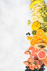 Raw fruits in rainbow colours, strawberries, mango, grapes, bananas, grapefruit on the off white table, copy space for text, top view, vertical, selective focus