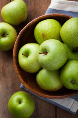 Ripe green apples in a wooden bowl on an old rustic table. Useful fruits on wooden background. Top view