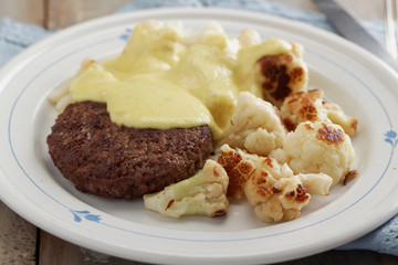 Meat burger with cauliflowers under cheese sauce