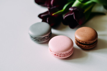 Pink, grey, brown macaroons with purple tulips on white background, copyspace, holiday concept