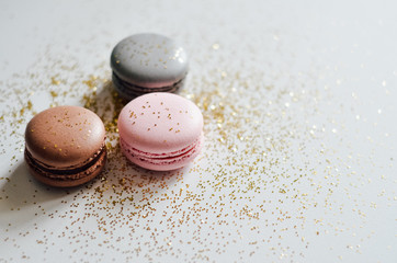 Pink, grey, brown macaroons with golden glitter on white background, copyspace, holiday concept