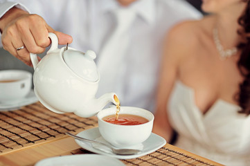 A newlywed couple drinking hot coffee or tea with sweet dessert in warm cozy cafe with wedding bouquet on the table. Atmoshere of happiness of new family and love tenderness