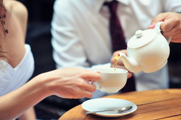 A newlywed couple drinking hot coffee or tea with sweet dessert in warm cozy cafe with wedding bouquet on the table. Atmoshere of happiness of new family and love tenderness