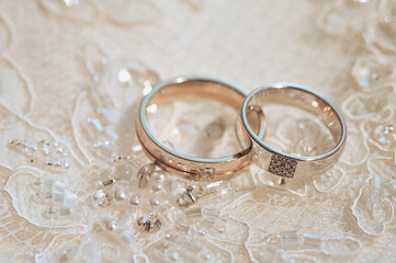 Obraz na płótnie Canvas Wedding rings, jewelry and symbols attributes taken with selective focus. Holiday, celebration. Macro. Blur. Bridal dress on background
