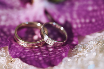 Wedding rings, jewelry and symbols attributes taken with selective focus. Holiday, celebration. Macro. Blur. Bridal bouquet on background