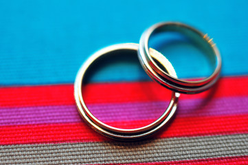 Wedding rings, jewelry and symbols attributes with blue and red taken with selective focus. Holiday, celebration. Macro. Blur. Bridal bouquet on background