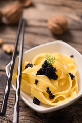 caviar pasta tagliatelle on a white bowl with wooden background. Close up