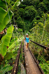 Fototapeta premium Young woman walking on suspension bridge over Wainibau stream, Lavena Coastal Walk, Taveuni Island, Fiji