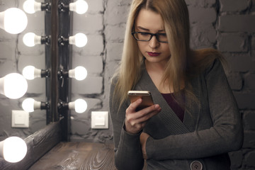 Attractive female in elegant dress reading news in network on cell telephone while is sitting in...