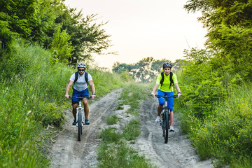 a woman and a man cycling in summer in the park on bicycles