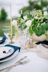 close-up glass glass on a tinned table with blue porcelain plates, silver cutlery and napkins, and a vase with tsirminina background of a green meadow