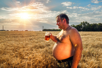A fat man drinking beer in the field of barley