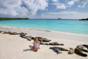 Young woman sitting with a group of Galapagos sea lions at Gardner Bay, Espanola Island, Galapagos National park, Ecuador