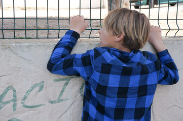 Blond boy looking through the hedge wearing blue shirt
