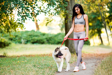 Naklejka na ściany i meble Sports woman walking with dog in the park.