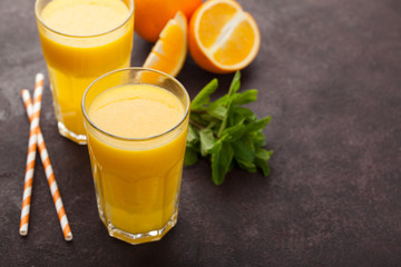 Two glasses of freshly squeezed orange juice and mint on a dark brown background. Top view with copy space