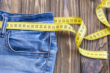 Healthy lifestyle and nutrition concept. Blue jeans with a measuring tape instead of a belt. 