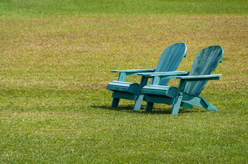Two blue adirondack chairs on a grassy lawn with negative space