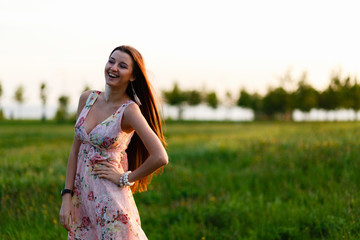 Girl in summer dress posing on sunset field background. Beautiful girl in meadow with sun rays young woman posing outdoors at nature with copy space