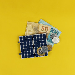 Solar panel with varied values of Brazilian money isolated in yellow background.
