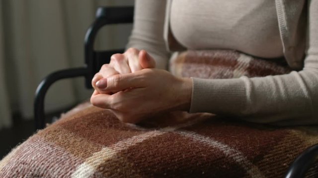 Woman nervously kneading numb cold hands sitting in wheelchair, feeling of doom