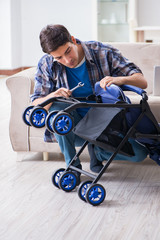 Young father assembling baby pram at home