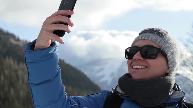 Young woman taking a self portrait with her smartphone in the mountains, Alps, Austria 