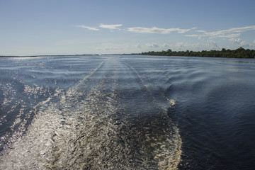 'Rio Negro' river, ripples in the water. Blue sky with clouds. Travelling through the Amazon rainforest by boat. Amazon / Brazil