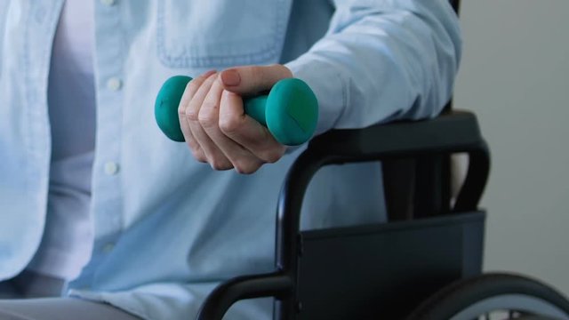 Woman in wheelchair trying to develop her arm after stroke, raising dumbbell