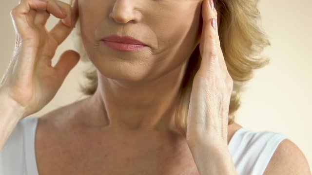 Woman pulling sagging skin on face with fingers, thinking about plastic surgery