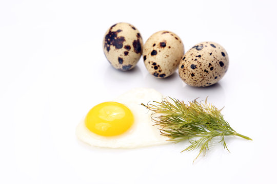 fried egg lying next to quail eggs on white background.
