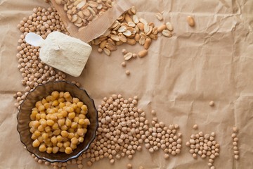 Copy space: boiled and raw chickpea, peanuts and protein powder laying on a piece of craft paper
