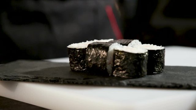 Panorama from right to left. The guy puts the Japanese rolls on the stand. Bare hands. Close-up.