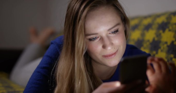 4K Happy young woman laying on the sofa, looking at her smartphone at night