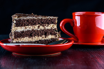 a piece of chocolate cake on a plate next to a cup of coffee, on a dark wooden background. Homemade baking.Close-up view.