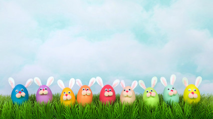 Colorful decorated Easter Eggs with bunny faces and ears lined up in a row on green grass, vintage sky background. Fun Easter concept. Banner format for social media and websites