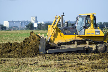 The yellow tractor with attached grederom makes ground leveling.