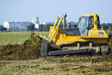 Obraz premium The yellow tractor with attached grederom makes ground leveling.