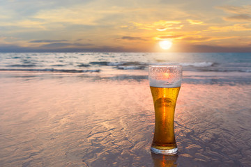 Glass of cold beer on the sea shore at the sunset. Relax on the beach.